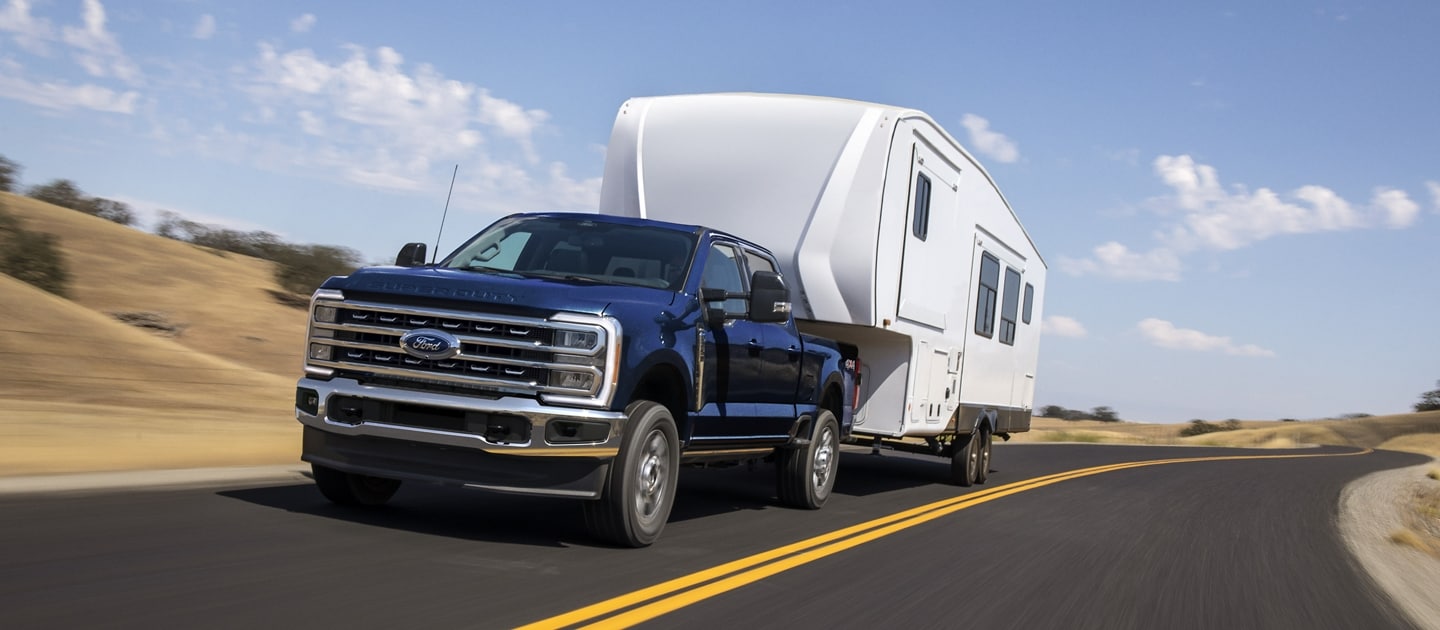 Modèle Ford Super Duty® XLT 2025 en bleu antimatière tirant une grande caravane sur une route pavée