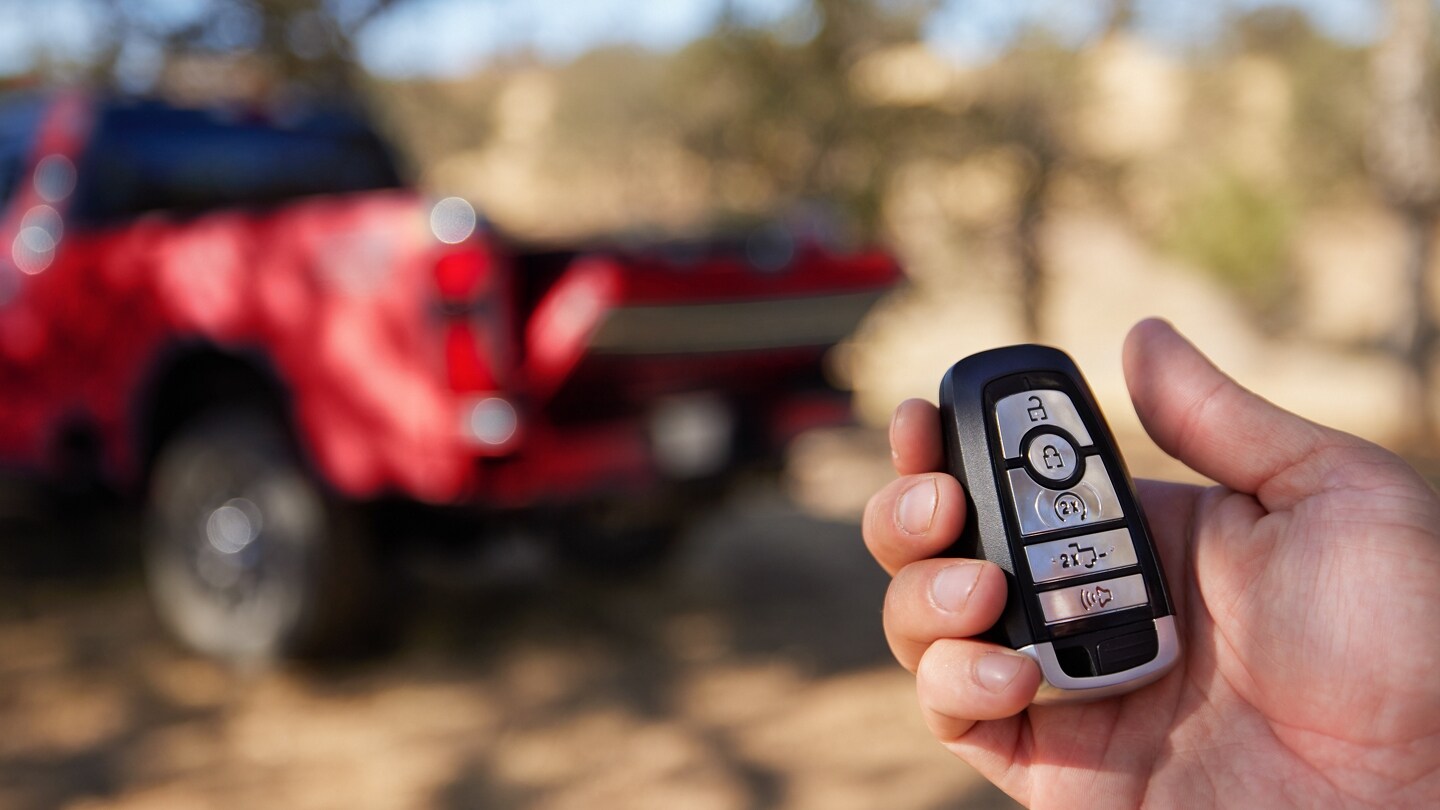 Main tenant un porte-clés avec un camion Ford Super Duty® King Ranch® rouge 2025 en arrière-plan