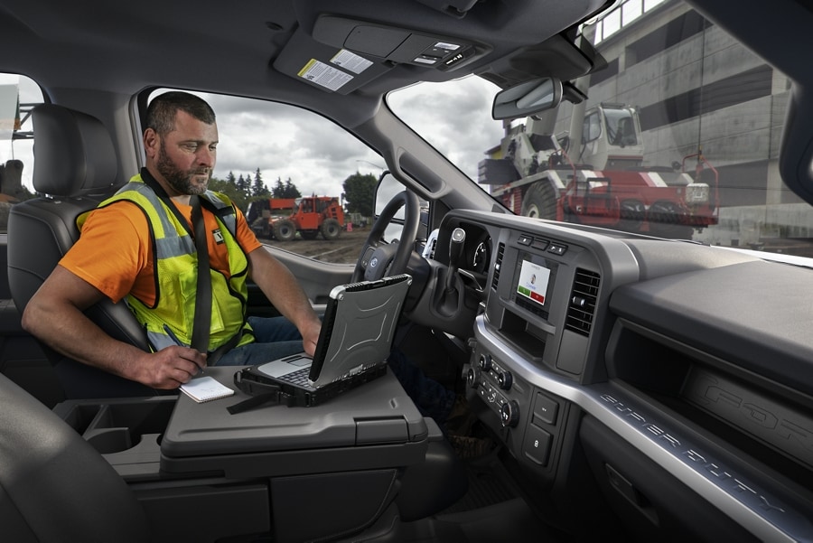 Homme travaillant sur un ordinateur portable à l’intérieur d’un Ford F-250® Super Duty® XL 2023 avec un chantier en arrière-plan