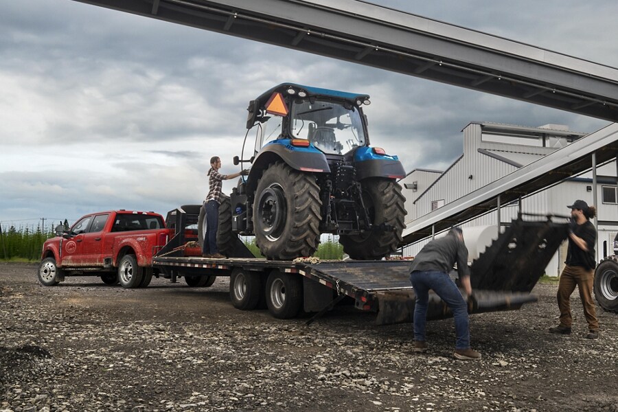 Hommes chargeant un tracteur sur une remorque attachée à un Ford F-450 Super Duty® XL 2023 à cabine 6 places près d’une usine de céréales