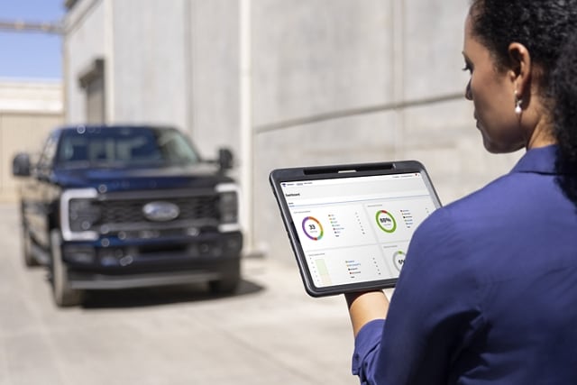 Femme regardant une tablette avec un modèle Ford Super Duty® XL STX® 2025 avec ensemble décor en stationné en arrière-plan