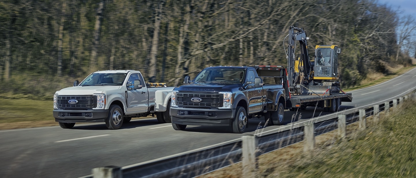 Ford Super Duty® F-350® XL RAJ 2025 en blanc Oxford et F-450® XL à RAJ en bleu antimatière circulant sur une route pavée