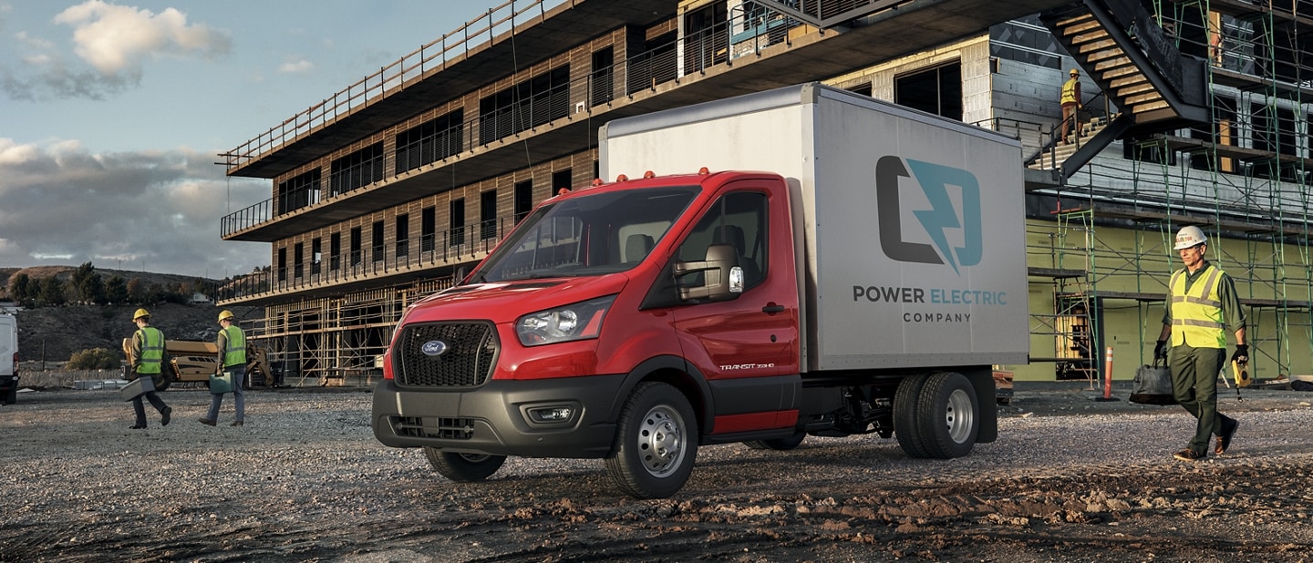 Modèle Ford Transit® châssis-cabine 2025 aménagé en camion fourgon stationné sur un chantier de construction avec trois travailleurs à proximité