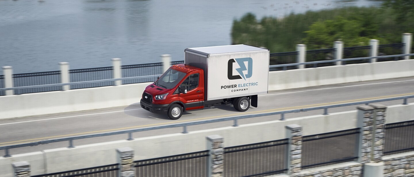 Modèle Ford Transit® châssis-cabine 2025 aménagé en camion fourgon conduit sur un pont avec un lac en arrière-plan