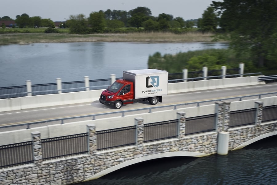Modèle Ford Transit® châssis-cabine 2025 aménagé en camion fourgon conduit sur un pont avec un lac en arrière-plan