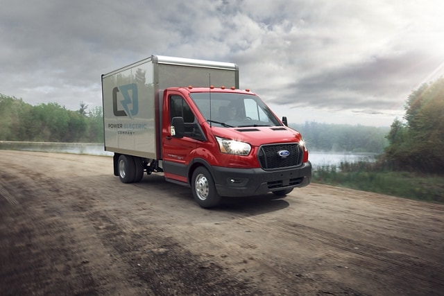 Modèle Ford Transit® châssis-cabine 2025 aménagé en camion fourgon conduit sur une route de terre près d’un lac