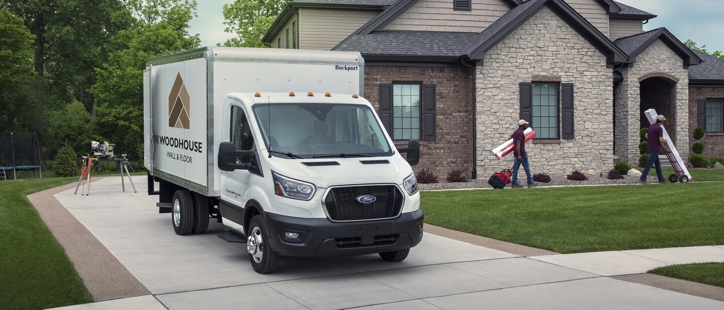 Modèle Ford Transit® châssis-cabine 2025 aménagé en camion fourgon stationné dans une entrée d’une maison avec des personnes y travaillant