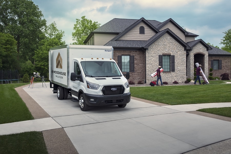 Modèle Ford Transit® châssis-cabine 2025 aménagé en camion fourgon stationné dans une entrée d’une maison avec des personnes y travaillant