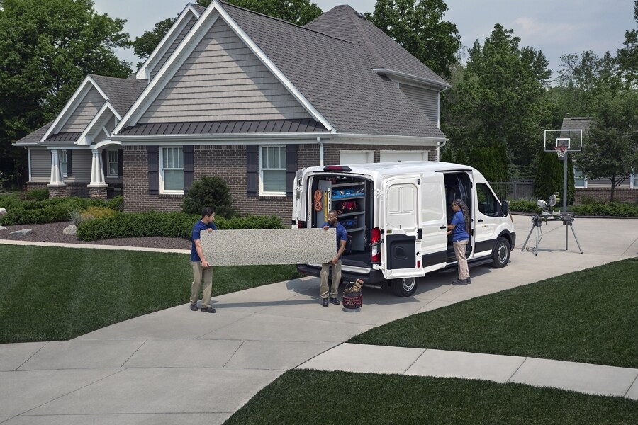 Une fourgonnette Ford Transit® 2023 stationnée dans une maison avec deux hommes à l’extérieur et une femme debout à une portière latérale ouverte