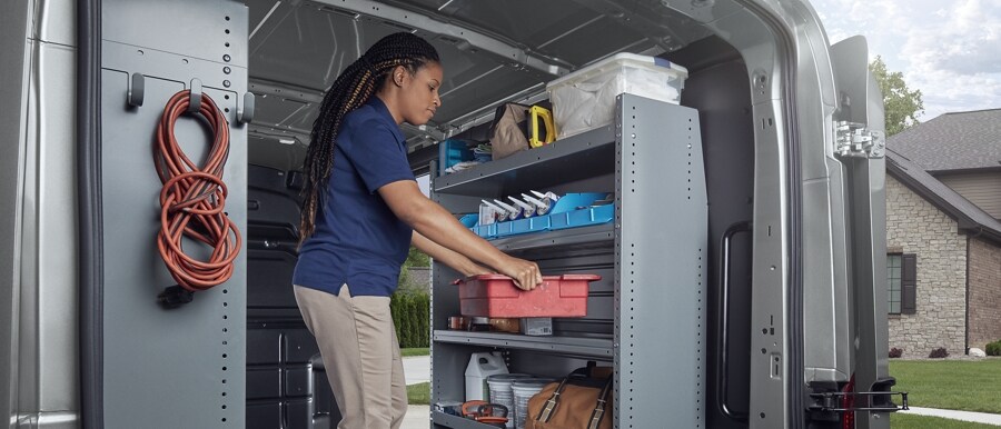 Photo de la zone de chargement d’une fourgonnette Ford Transit® 2023 avec une femme mettant un conteneur sur des tablettes