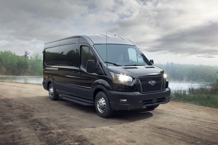 Une fourgonnette Ford Transit® 2024 en noir agate avec système de traction intégrale intelligente emprunte une route de terre
