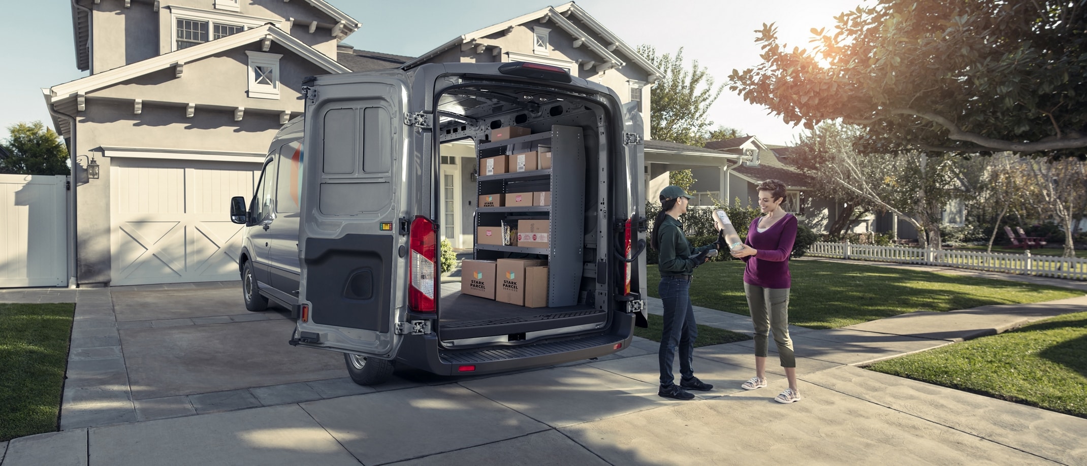 Une fourgonnette Ford Transit® 2025 stationnée dans une entrée avec les portières arrière ouvertes alors qu’un livreur dépose un colis