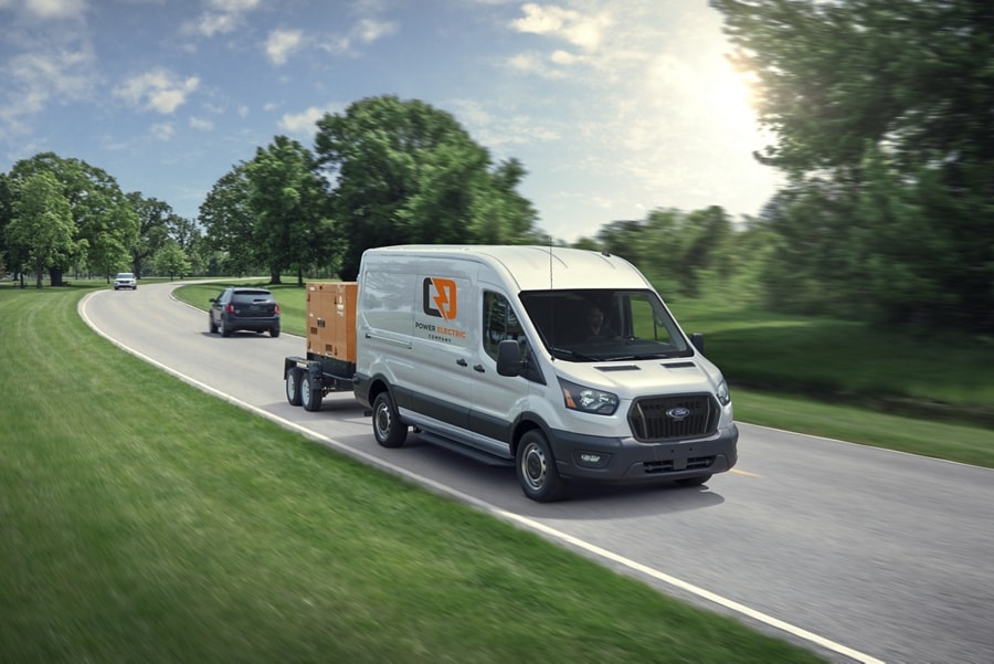 Une fourgonnette Ford Transit® 2025 circulant sur une route tirant une grande génératrice électrique